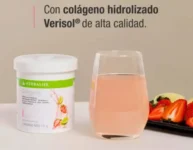 La imagen muestra un envase blanco de Collagen Drink, un producto para mejorar la salud de la piel. En el frente del envase está el nombre del producto en letras destacadas. El fondo cafe, al ladio un vaso con colageno junto a unas frutillas